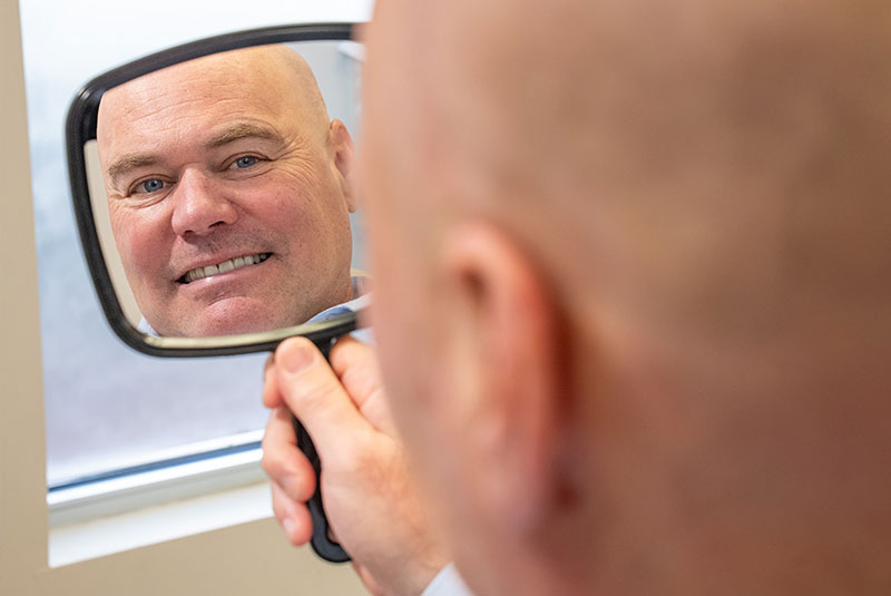 patient looking in handheld mirror and smiling