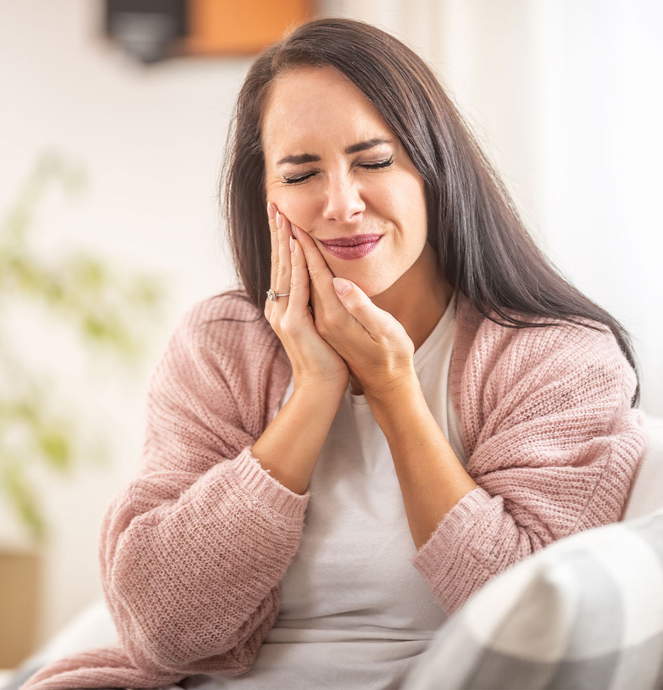 womensits at home with a toothache holding her right cheek with hands